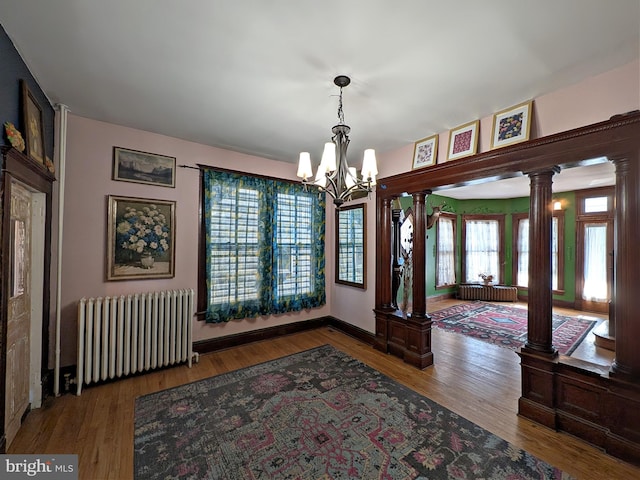 interior space featuring decorative columns, radiator, wood finished floors, a chandelier, and baseboards