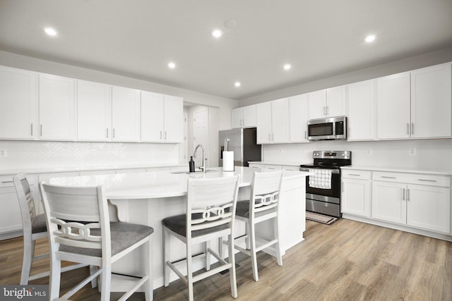 kitchen featuring a center island with sink, stainless steel appliances, light countertops, light wood-style flooring, and white cabinets