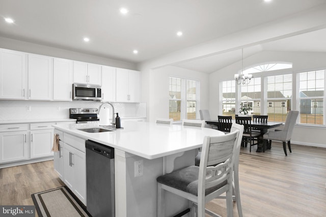 kitchen featuring light wood-style flooring, appliances with stainless steel finishes, a sink, vaulted ceiling, and a notable chandelier