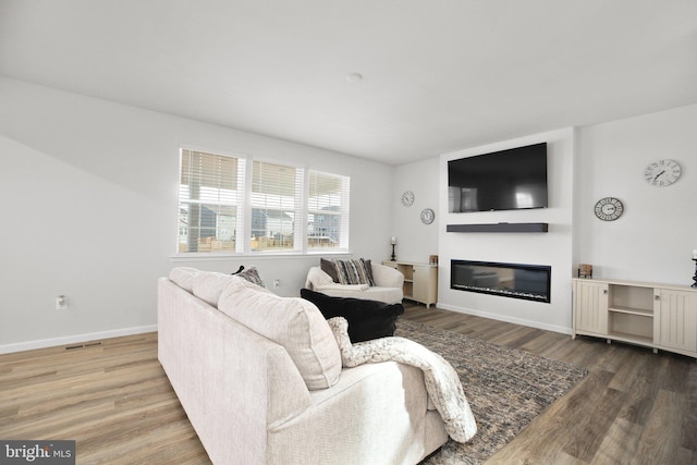 living area featuring a glass covered fireplace, visible vents, baseboards, and wood finished floors