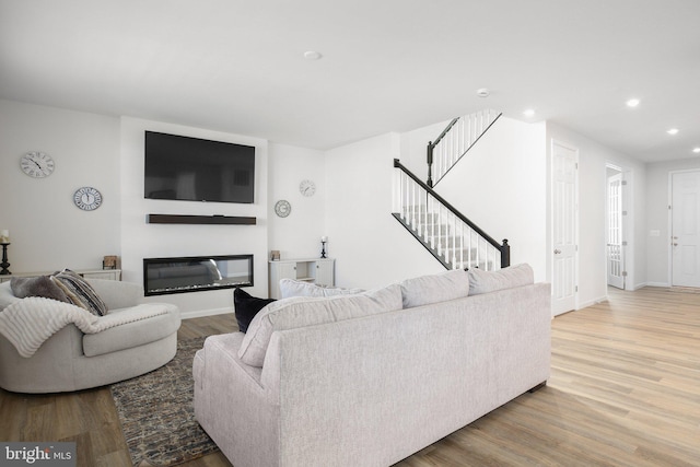 living area with a glass covered fireplace, stairway, recessed lighting, and wood finished floors