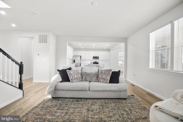 living room with light wood finished floors, baseboards, stairs, and visible vents