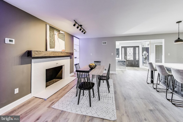 dining area featuring rail lighting, built in features, a high end fireplace, and light hardwood / wood-style floors