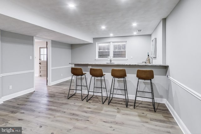 kitchen featuring a kitchen breakfast bar, light stone countertops, light hardwood / wood-style floors, and kitchen peninsula