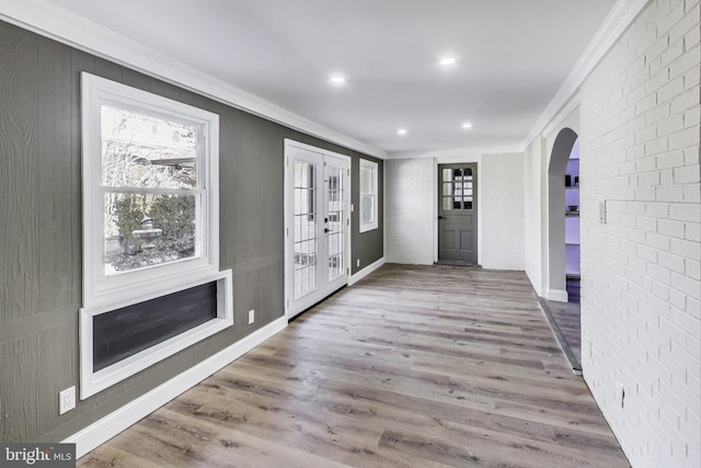 foyer entrance featuring wood-type flooring, ornamental molding, and brick wall