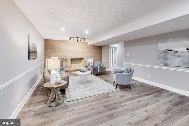 living room featuring hardwood / wood-style floors, track lighting, a brick fireplace, and brick wall