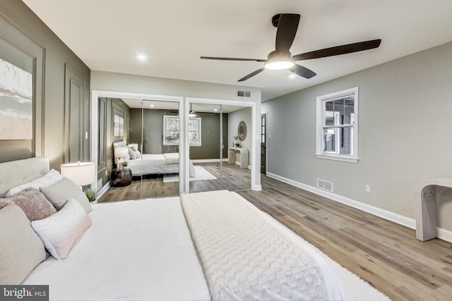 bedroom featuring ceiling fan, light hardwood / wood-style flooring, and two closets