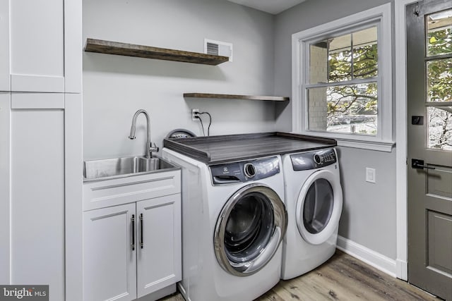 clothes washing area with cabinets, washing machine and dryer, sink, and light wood-type flooring