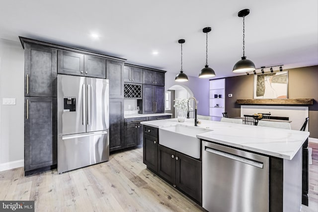 kitchen with sink, stainless steel appliances, light stone counters, a center island with sink, and decorative light fixtures