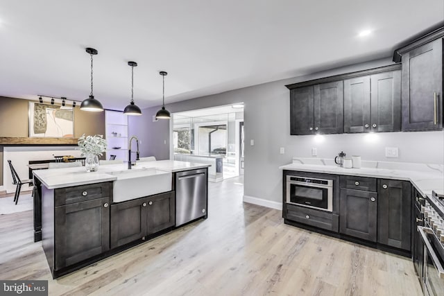 kitchen featuring decorative light fixtures, dishwasher, sink, light stone countertops, and light wood-type flooring