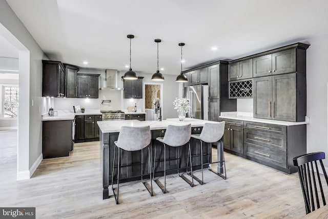 kitchen featuring hanging light fixtures, high quality appliances, light hardwood / wood-style floors, a center island with sink, and wall chimney exhaust hood