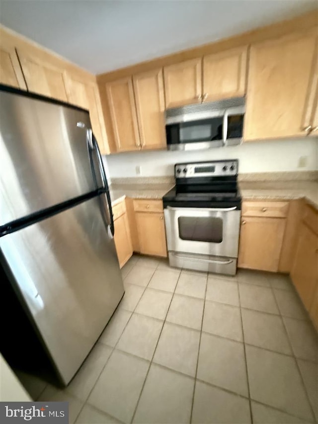 kitchen with appliances with stainless steel finishes, light tile patterned floors, light countertops, and light brown cabinetry