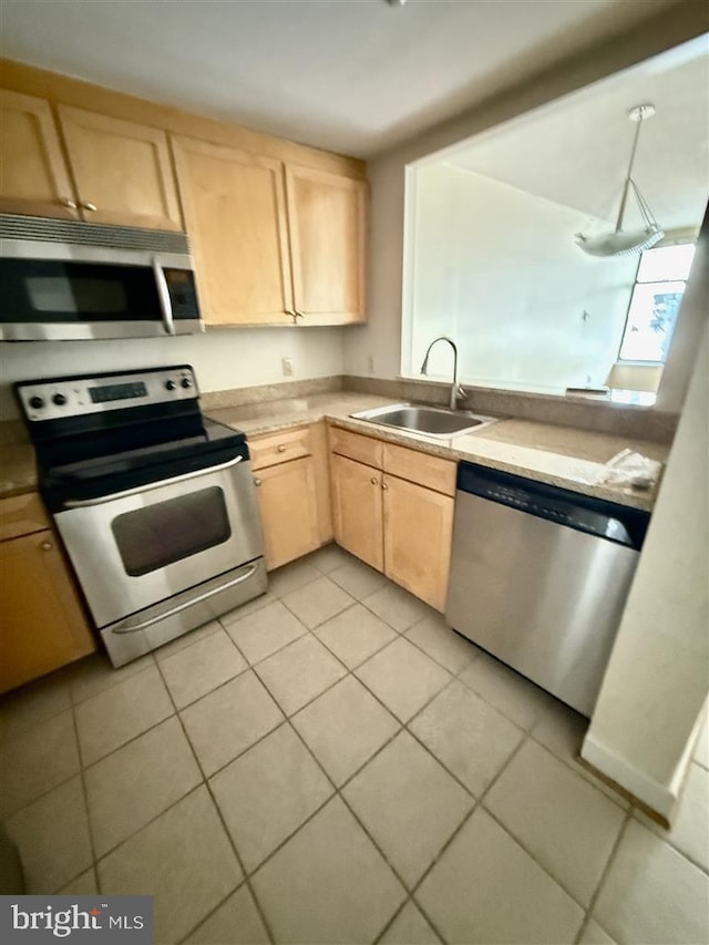 kitchen with light countertops, light brown cabinetry, appliances with stainless steel finishes, light tile patterned flooring, and a sink