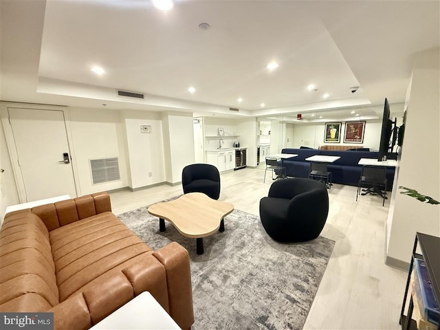 living room with a tray ceiling, light wood-style flooring, visible vents, and recessed lighting