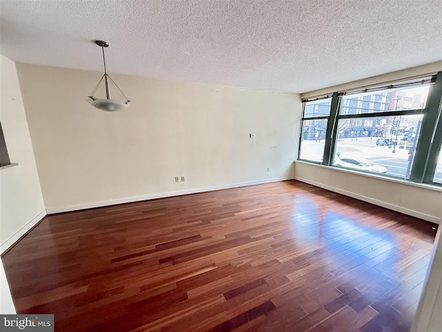 unfurnished room with a textured ceiling, wood finished floors, and baseboards