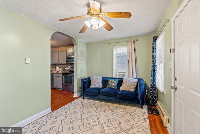 living room with baseboard heating, ceiling fan, a textured ceiling, and light wood-type flooring