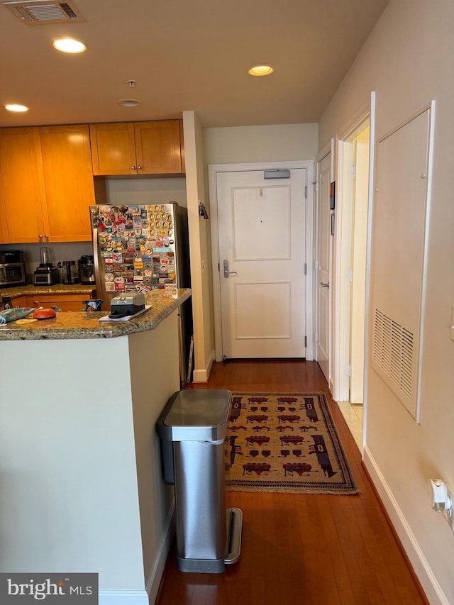 kitchen with dark wood-type flooring, stainless steel fridge, and stone counters