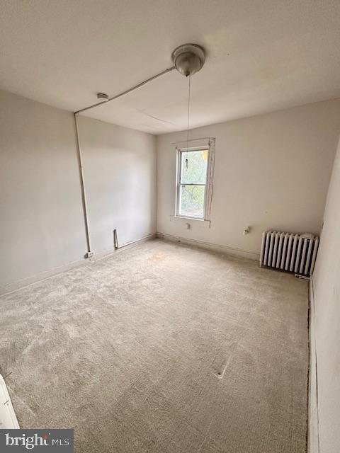 unfurnished room with baseboards, radiator, and carpet flooring