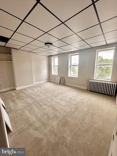 interior space with baseboards, a drop ceiling, radiator heating unit, and carpet floors