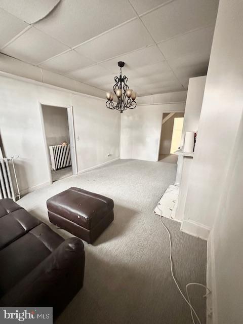 carpeted living room featuring a drop ceiling, an inviting chandelier, and radiator heating unit