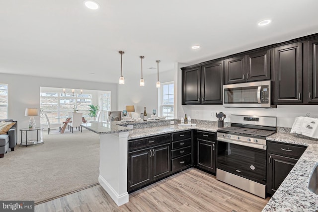 kitchen with stainless steel appliances, kitchen peninsula, light stone counters, and decorative light fixtures