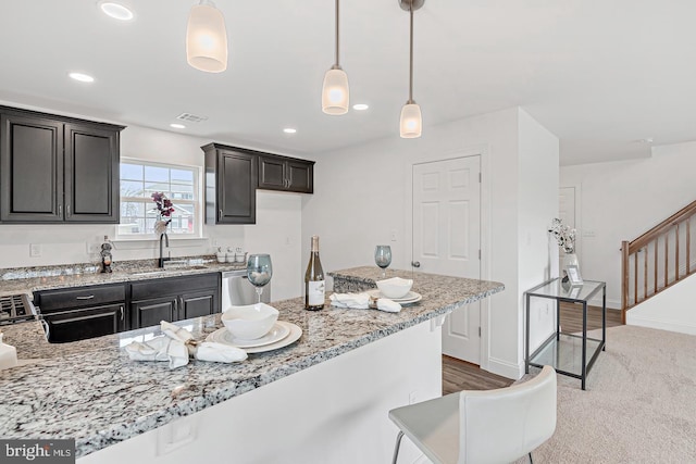 kitchen featuring sink, light stone counters, light carpet, hanging light fixtures, and stove