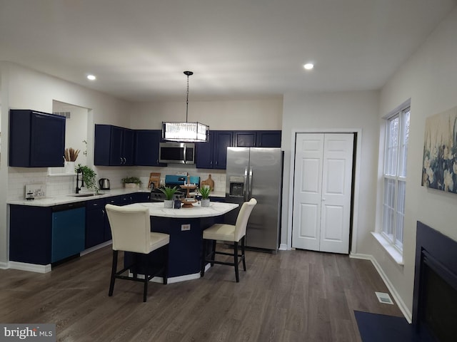 kitchen featuring a breakfast bar, appliances with stainless steel finishes, hanging light fixtures, a center island, and blue cabinets