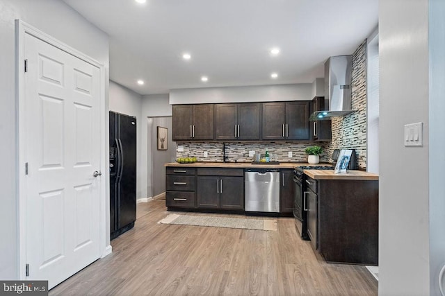 kitchen featuring dark brown cabinetry, wall chimney exhaust hood, butcher block counters, light wood-type flooring, and black appliances