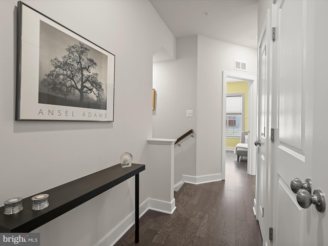 hallway with visible vents, an upstairs landing, baseboards, and dark wood-style floors