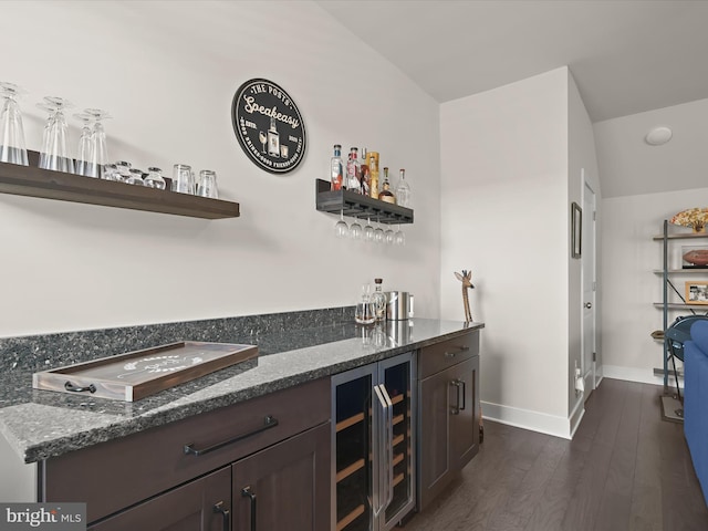 bar featuring beverage cooler, dark wood-style floors, baseboards, a bar, and vaulted ceiling