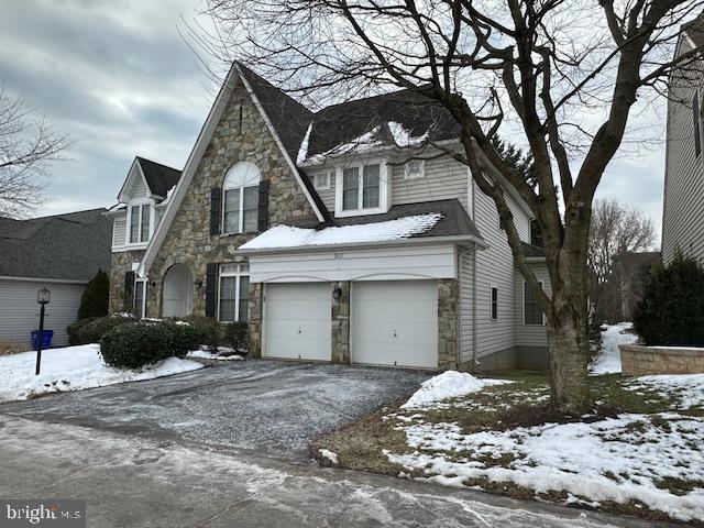 view of front of property featuring an attached garage, driveway, and stone siding