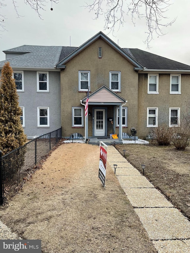 view of front facade with stucco siding, covered porch, and fence