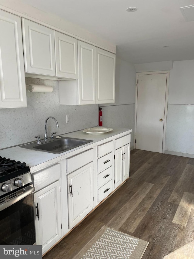 kitchen with dark wood finished floors, light countertops, white cabinetry, and a sink