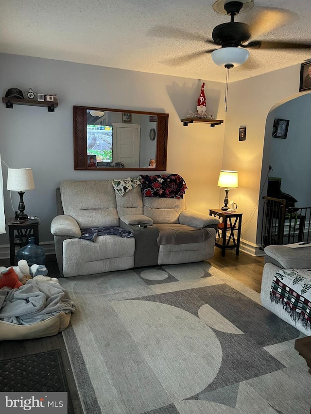 living area with arched walkways, a textured ceiling, a ceiling fan, and wood finished floors