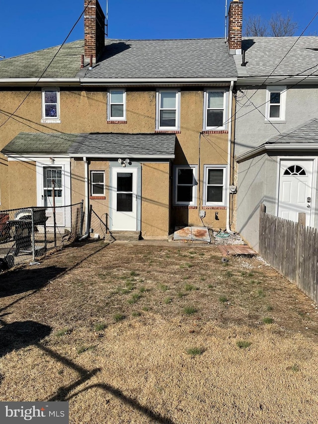 back of property with a shingled roof, stucco siding, fence, and a chimney