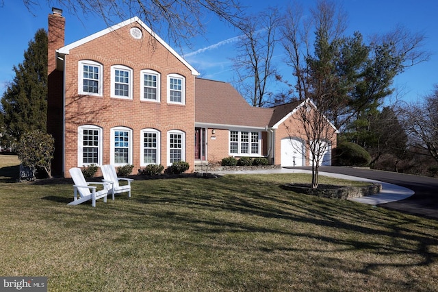 colonial house featuring a garage, brick siding, a chimney, and a front yard