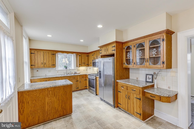 kitchen with tasteful backsplash, light stone countertops, stainless steel appliances, and sink