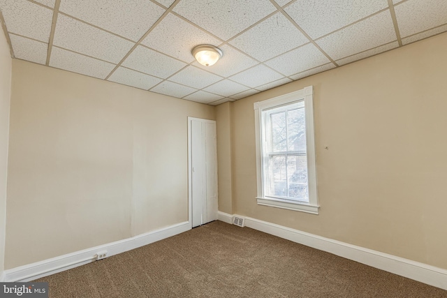 carpeted empty room featuring a drop ceiling