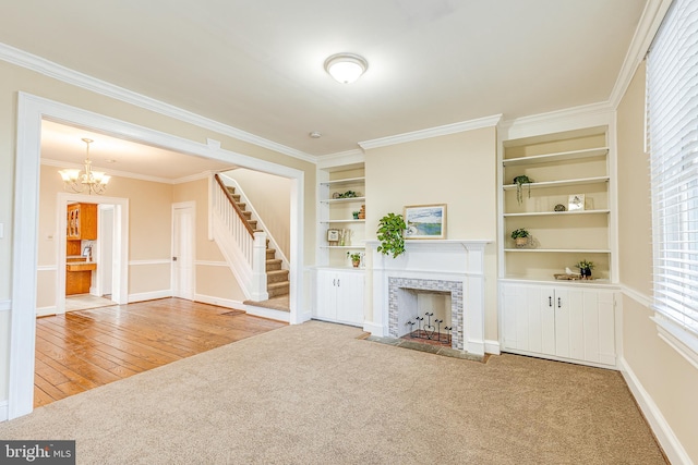 unfurnished living room with built in shelves, an inviting chandelier, ornamental molding, carpet flooring, and a fireplace