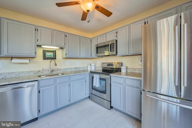 kitchen featuring appliances with stainless steel finishes, a ceiling fan, a sink, and light stone countertops