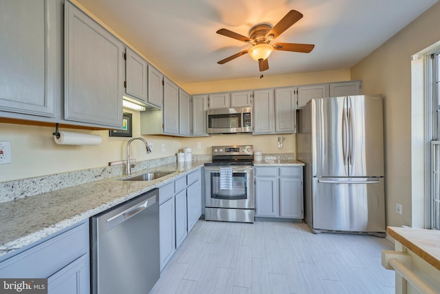 kitchen with ceiling fan, light stone countertops, gray cabinets, stainless steel appliances, and a sink