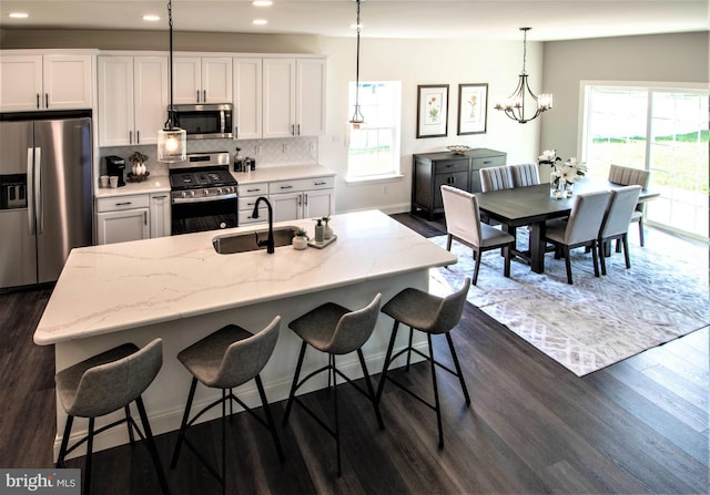 kitchen featuring pendant lighting, stainless steel appliances, tasteful backsplash, an island with sink, and white cabinets