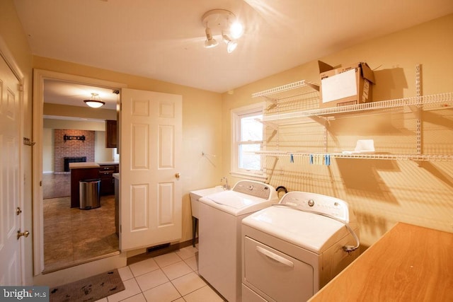 clothes washing area featuring a brick fireplace, light tile patterned floors, and washing machine and clothes dryer