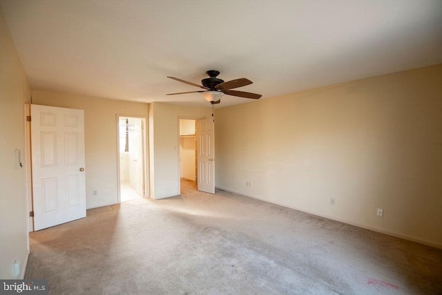 unfurnished bedroom featuring a closet, a walk in closet, light colored carpet, and ensuite bath