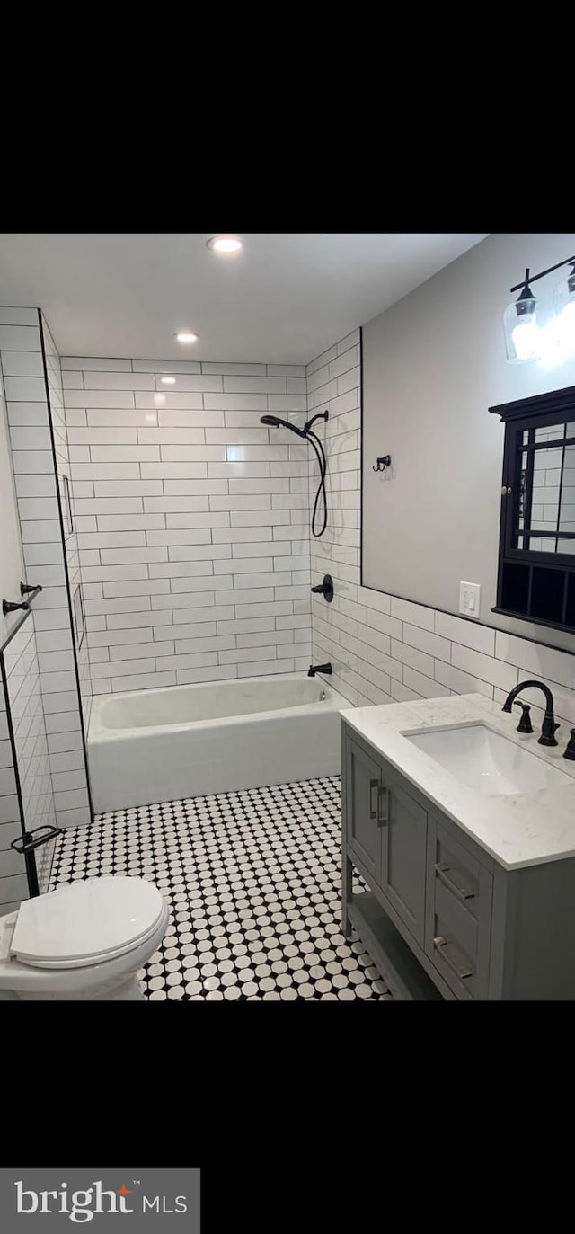 full bathroom featuring tile walls, vanity, tiled shower / bath combo, and toilet