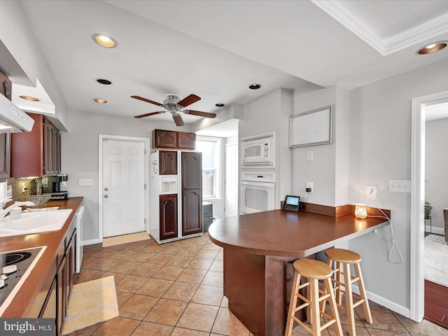 kitchen featuring a breakfast bar, sink, light tile patterned floors, kitchen peninsula, and white appliances