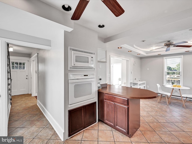 kitchen with a tray ceiling, light tile patterned floors, ceiling fan, kitchen peninsula, and white appliances