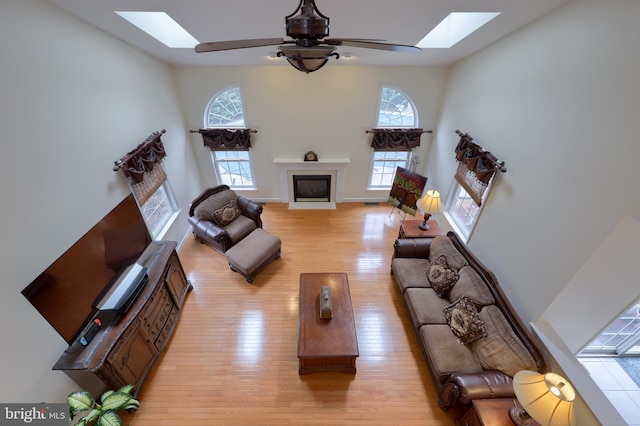 living room featuring a skylight, a fireplace, light wood finished floors, and a ceiling fan