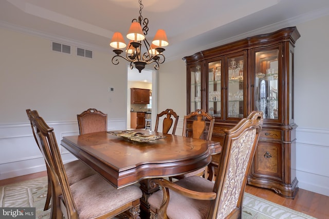 dining space with a wainscoted wall, visible vents, light wood-style floors, ornamental molding, and an inviting chandelier