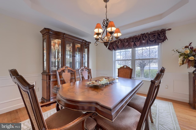 dining space featuring light wood finished floors, a decorative wall, a notable chandelier, and a wainscoted wall